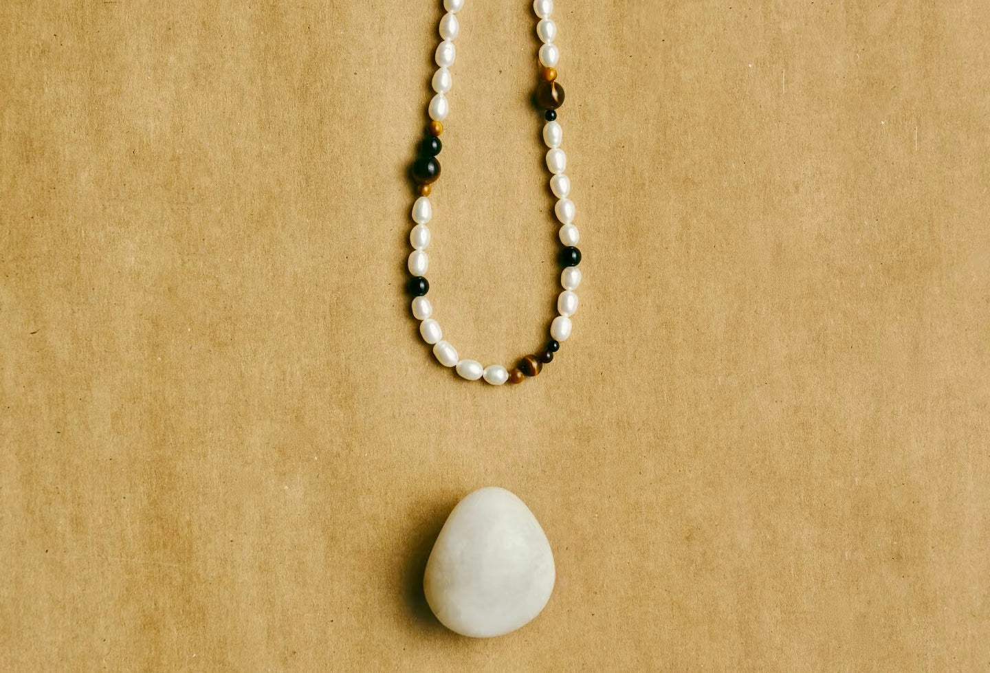 Beaded pearl necklace with alternating white and dark beads featuring a large smooth stone pendant on a beige background