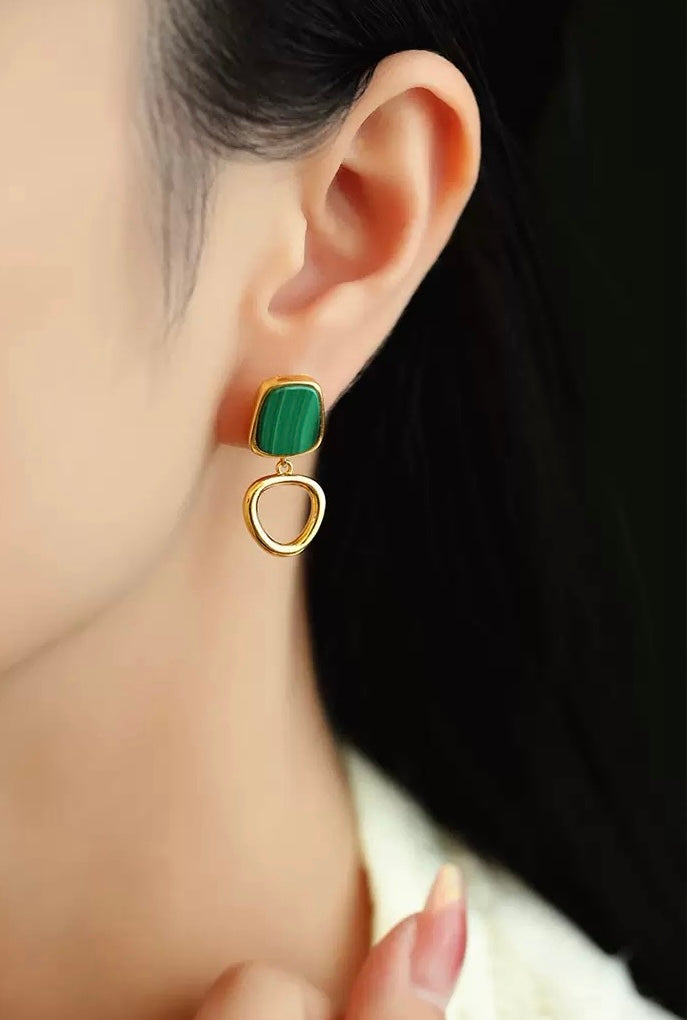Green and gold earring worn by a person