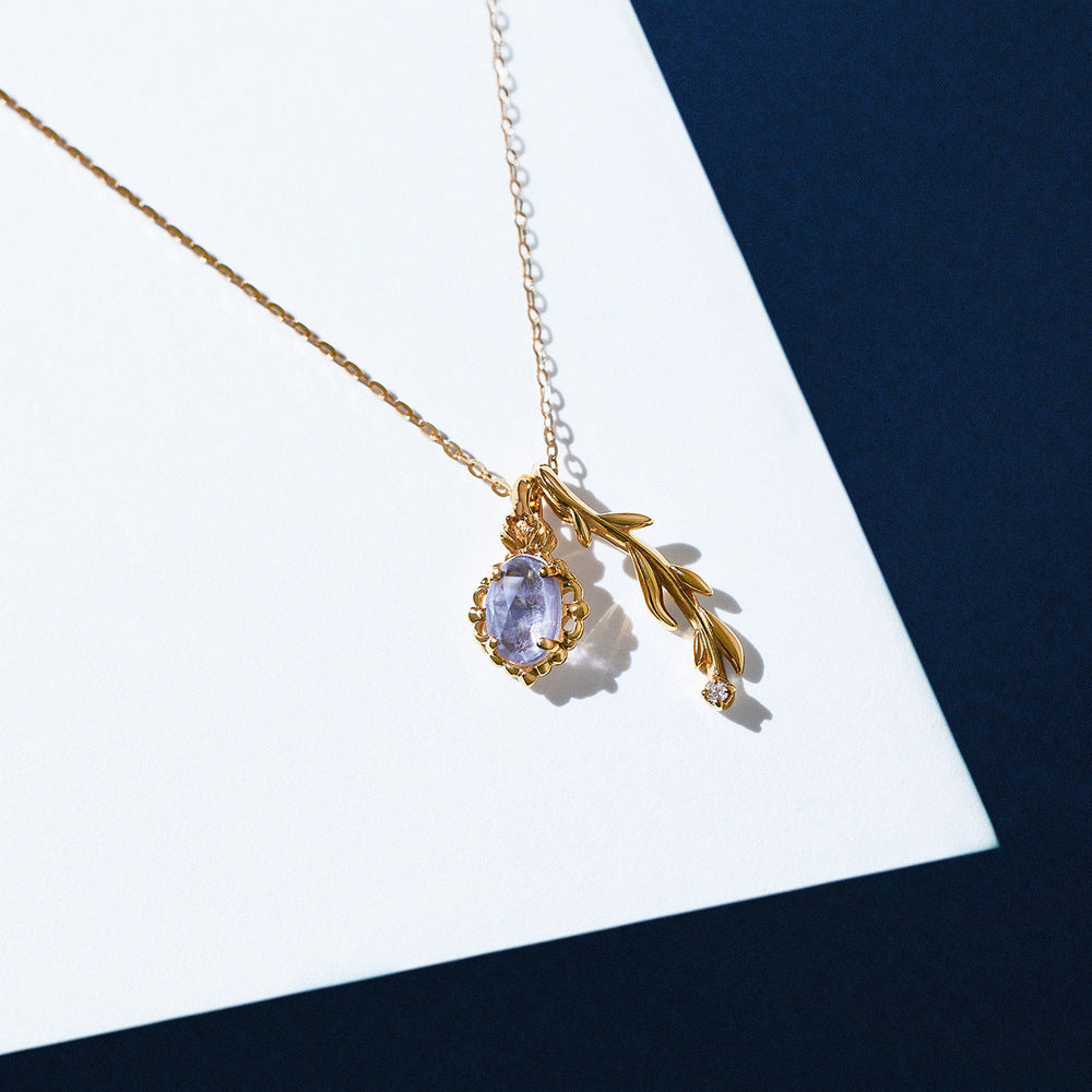 Gold necklace with a pendant featuring a teardrop-shaped gemstone on a white and blue background