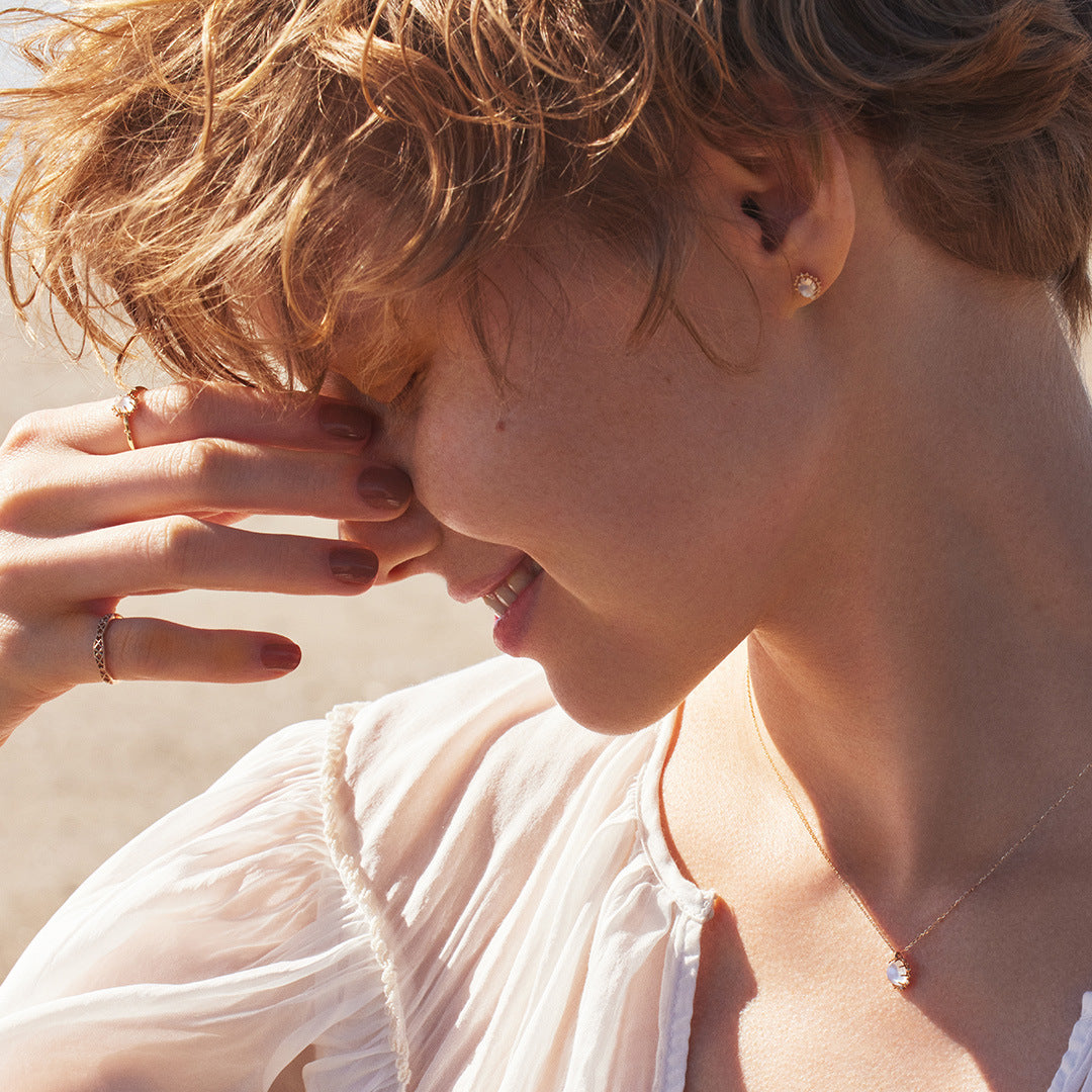 Close-up of a person with short hair wearing earrings and a necklace, with a blurred background.