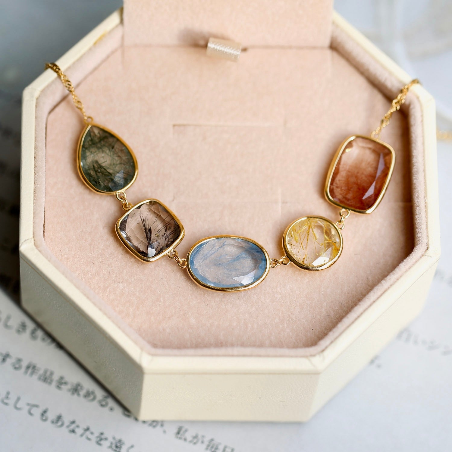 Candy-coloured rutilated quartz bracelet with five natural gemstones in green, brown, blue, yellow, and orange tones, set in 18K gold-plated 925 sterling silver on a velvet jewellery box