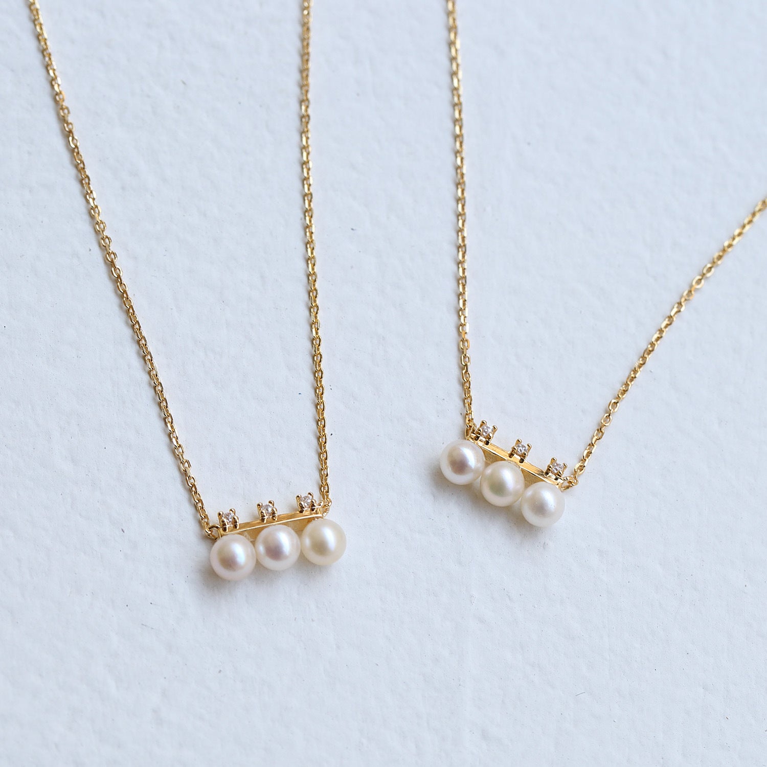 Two pearl necklaces on gold chains against a light blue background from Gembee Jewellery