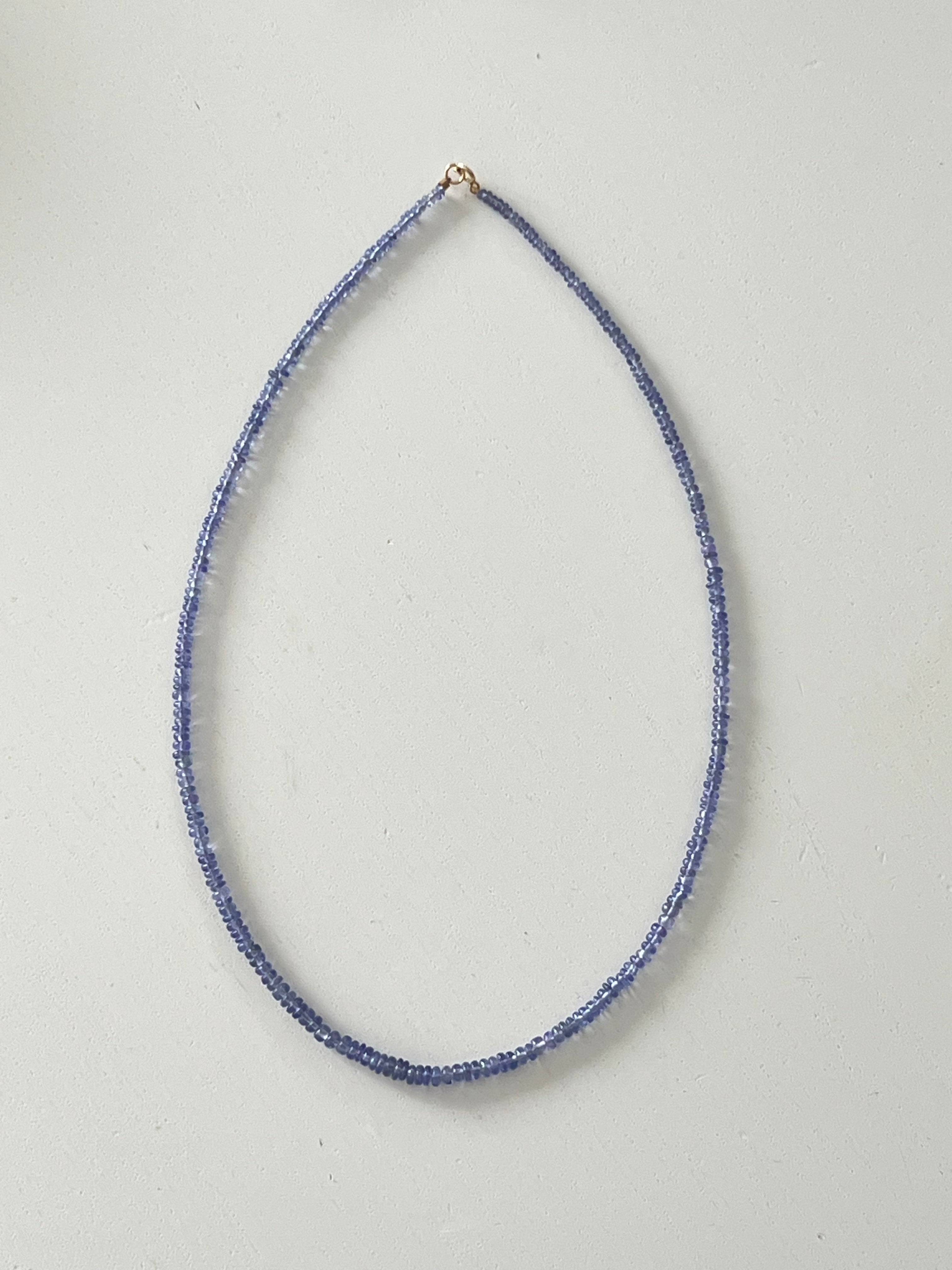 Thin tanzanite beaded necklace on a light gray background