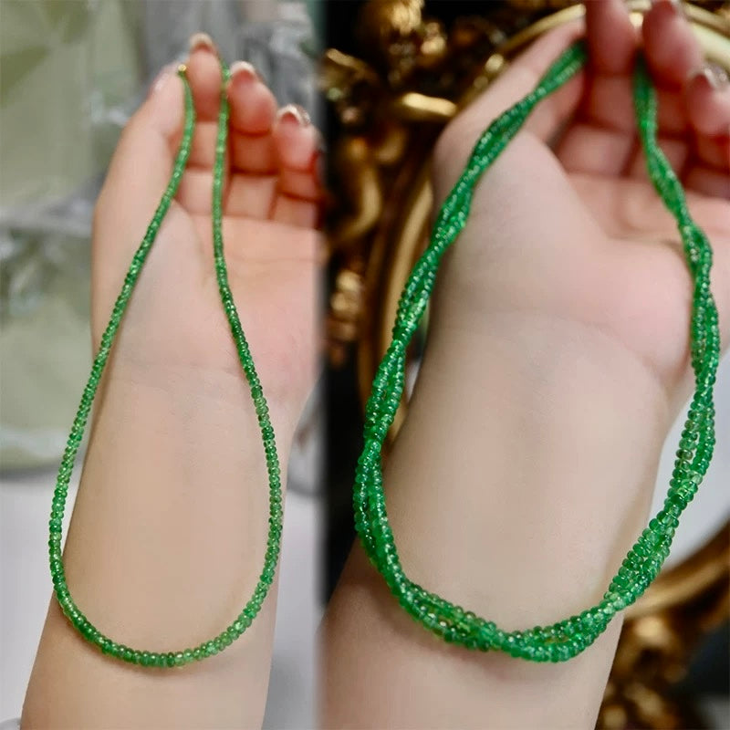 Green beaded necklace held between two hands with a blurred background