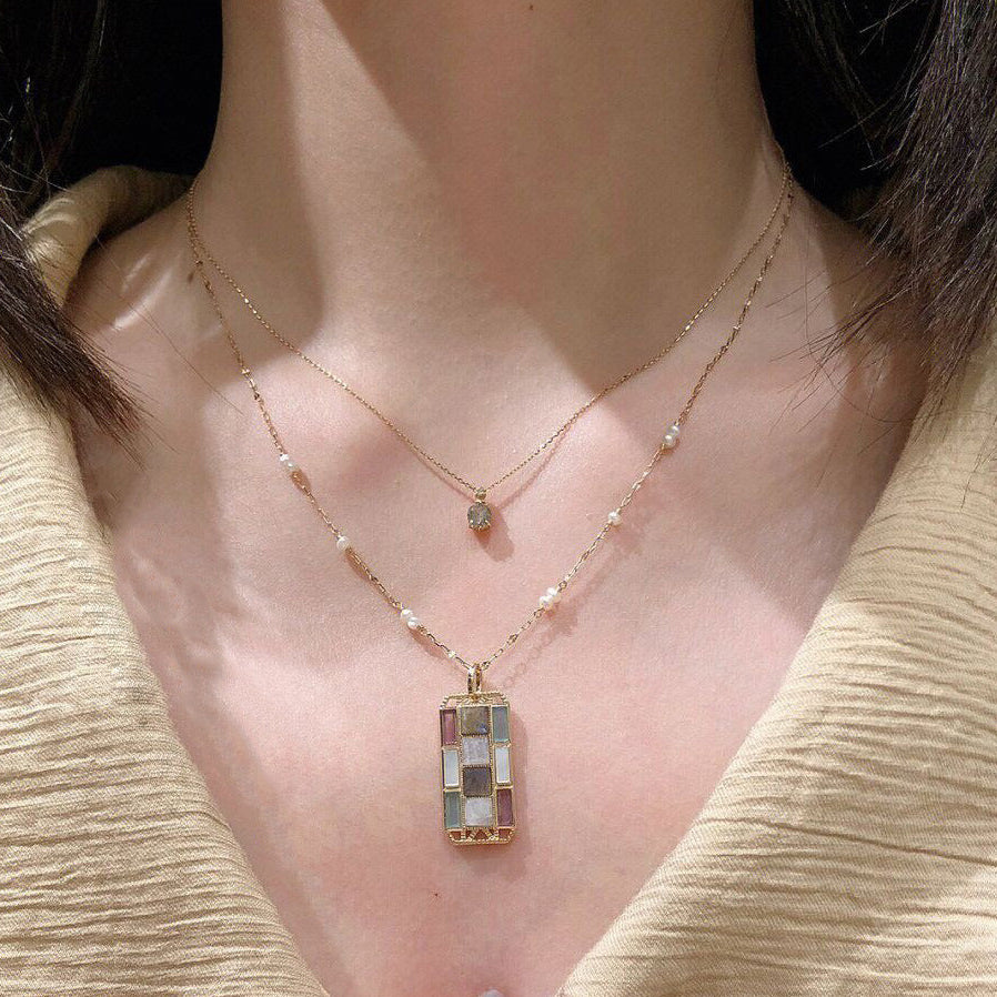 Necklace with a rectangular pendant worn by a person in a beige outfit.