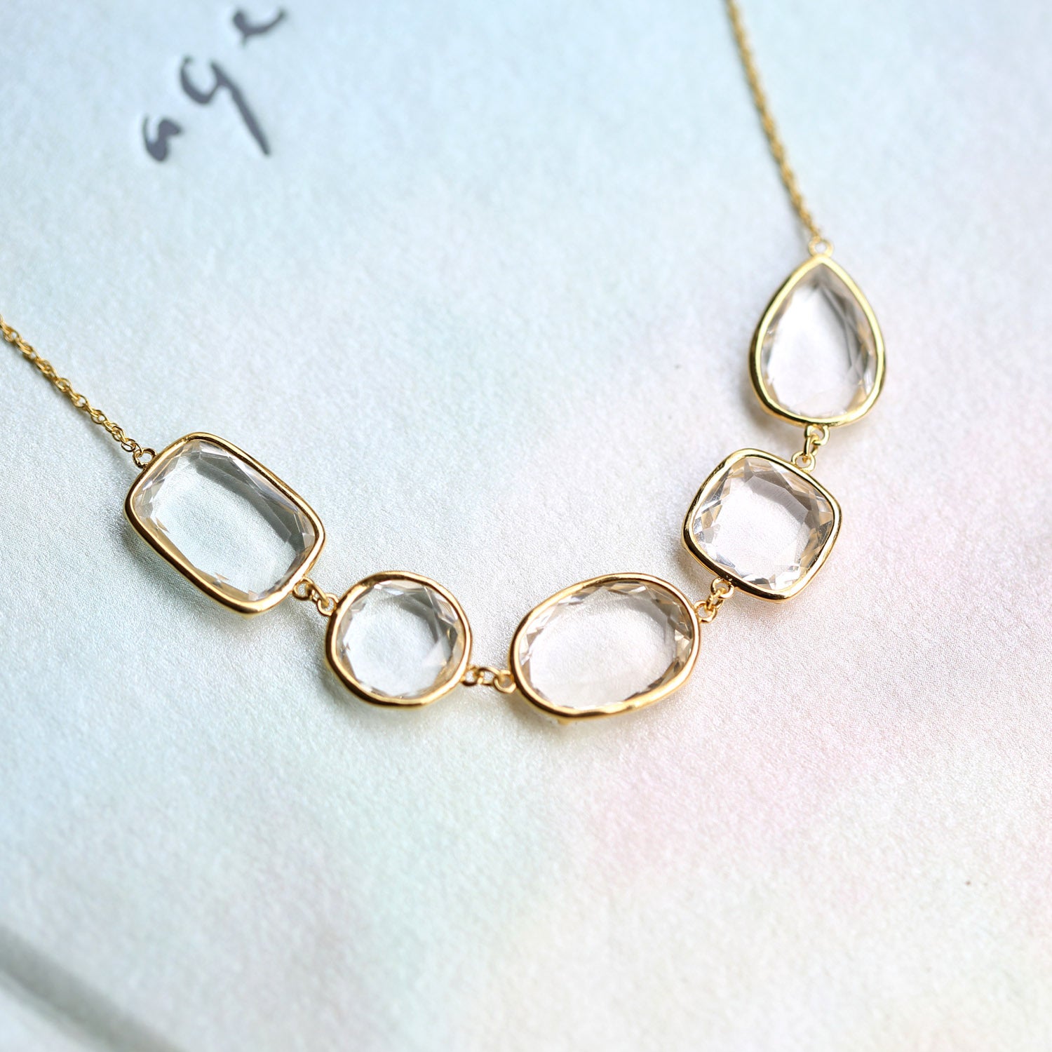 Gold bracelets with clear teardrop-shaped pendants on a light blue background