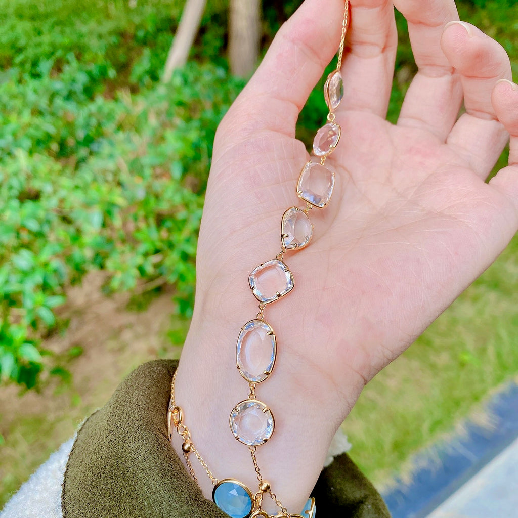 Hand wearing a gold bracelet with gemstones against a natural background
