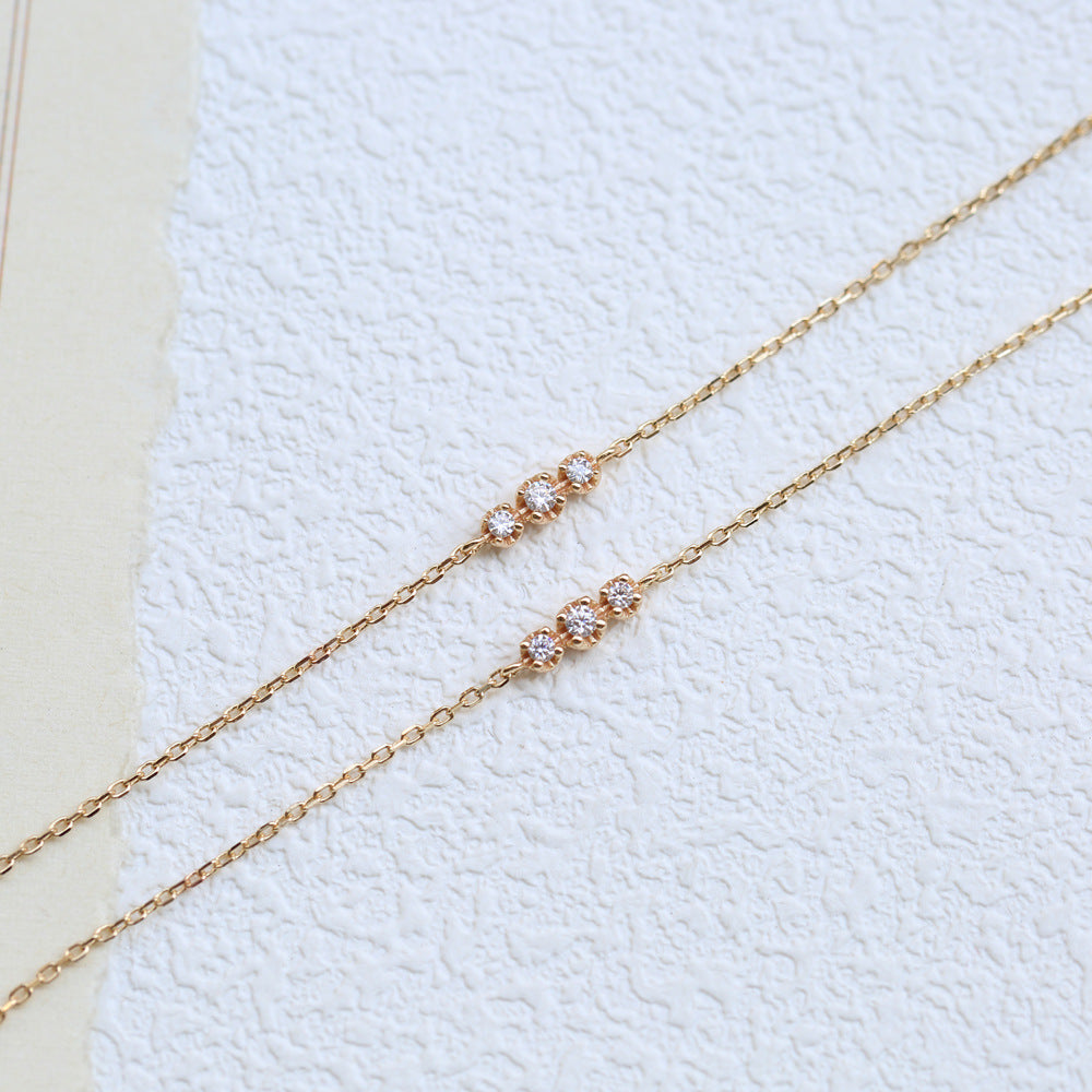 Gold chain bracelet with small diamonds on a textured white background from The GemBee Jewellery.
