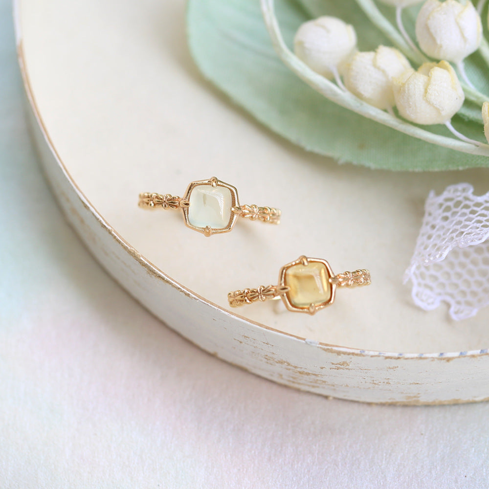 Two gold rings with gemstones on a white plate with flowers in the background