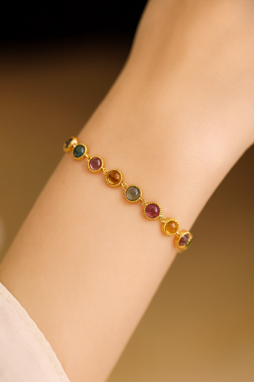 Gold bracelet with multicoloured gemstones on a wrist against a brown background