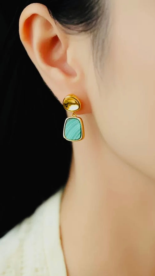 Gold earring with a Malachite stone worn by a person against a neutral background