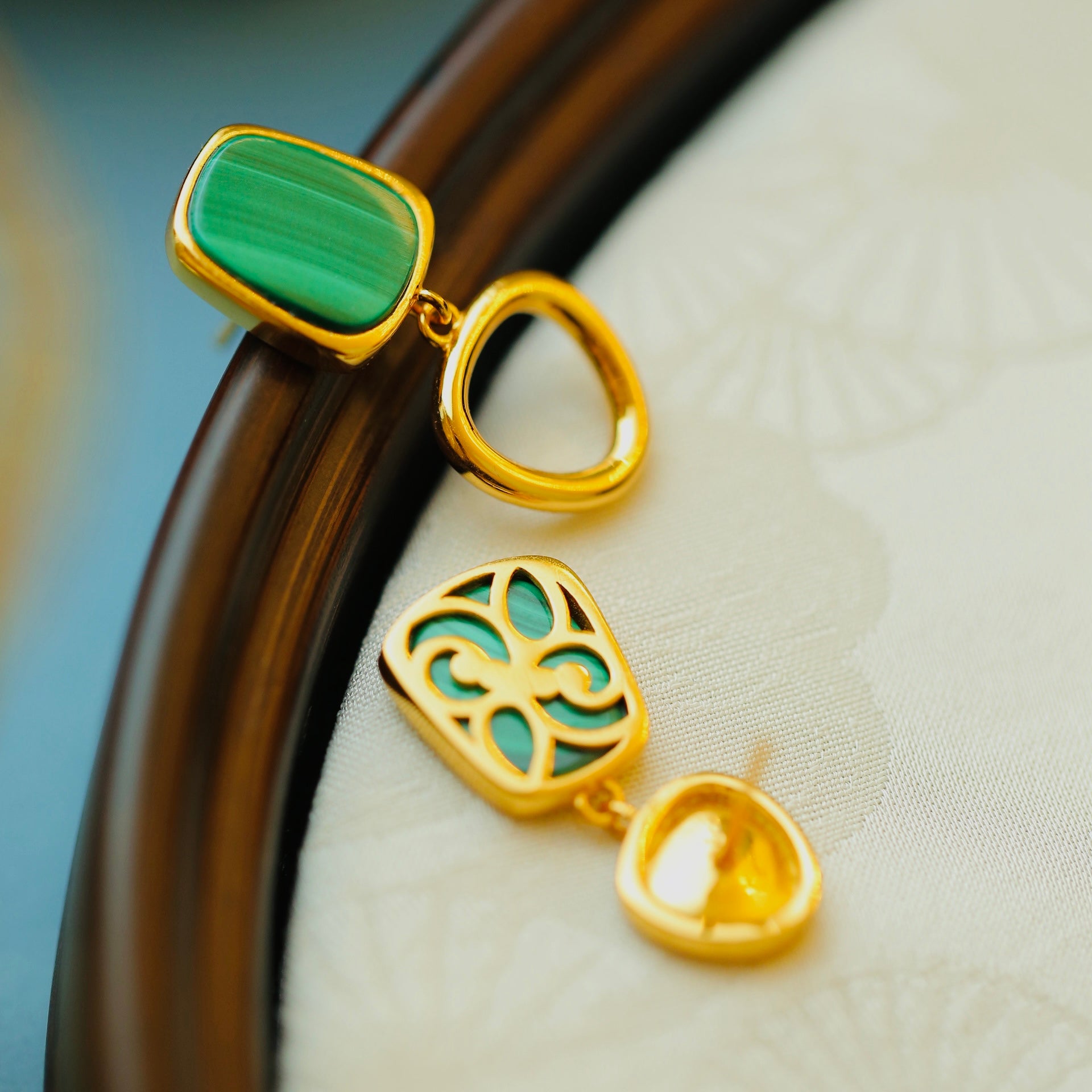 Gold earrings with green gemstones on a fabric background