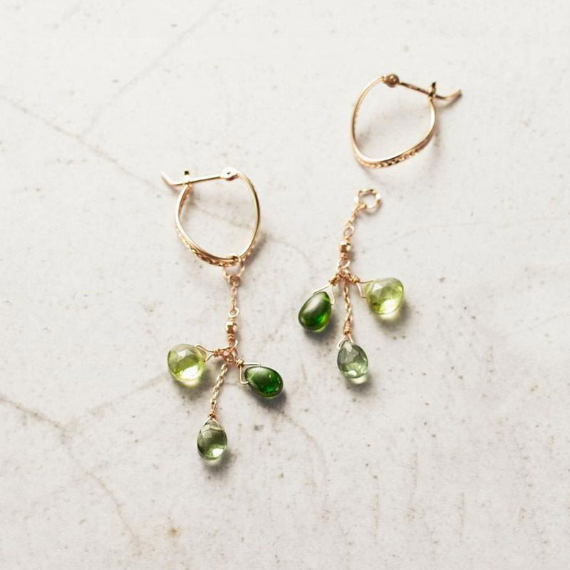 Gold hoop earrings with green gemstone drops on a light background