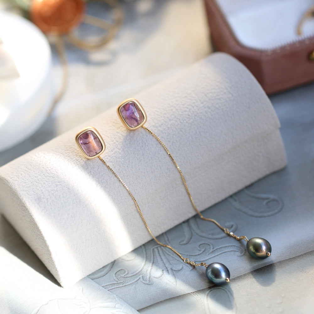 Gold necklace with pink gemstones and black pearls on a white cushion