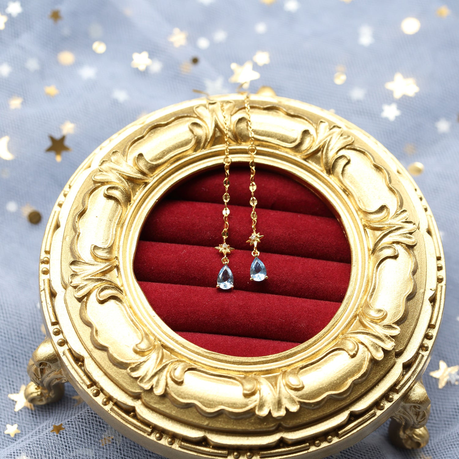 Gold jewelry box with red interior holding earrings on a starry background from Gembee Jewellery
