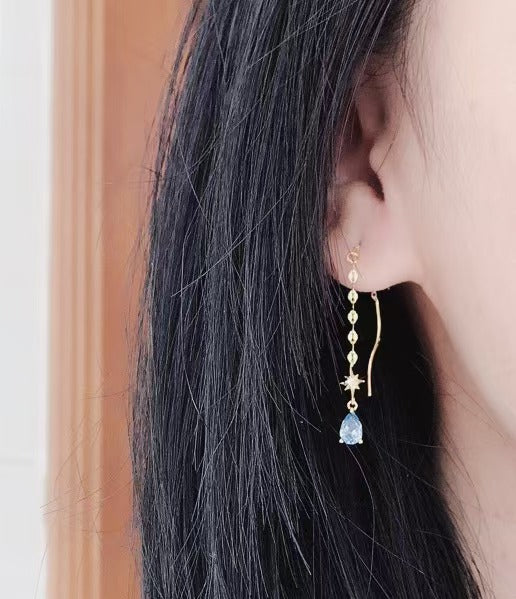 Close-up of an ear wearing a gold earring with a blue gemstone from Gembee Jewellery