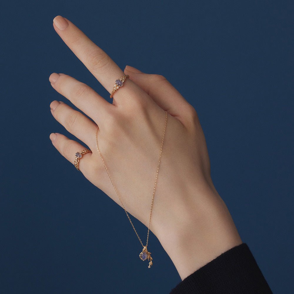 Hand wearing a gold necklace and ring against a dark blue background