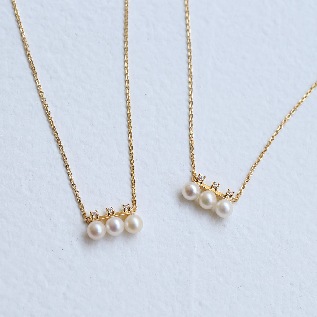 Two pearl necklaces on gold chains against a light blue background from Gembee Jewellery