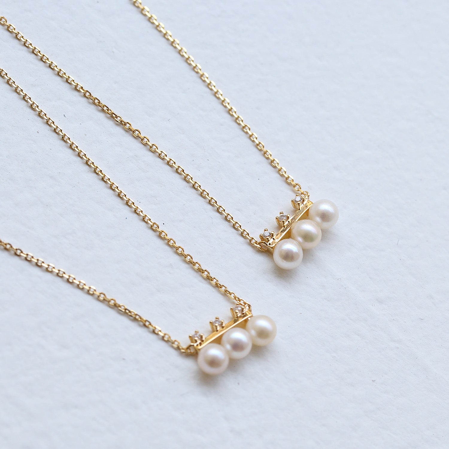 Gold necklaces with pearl pendants on a light blue background from Gembee Jewellery