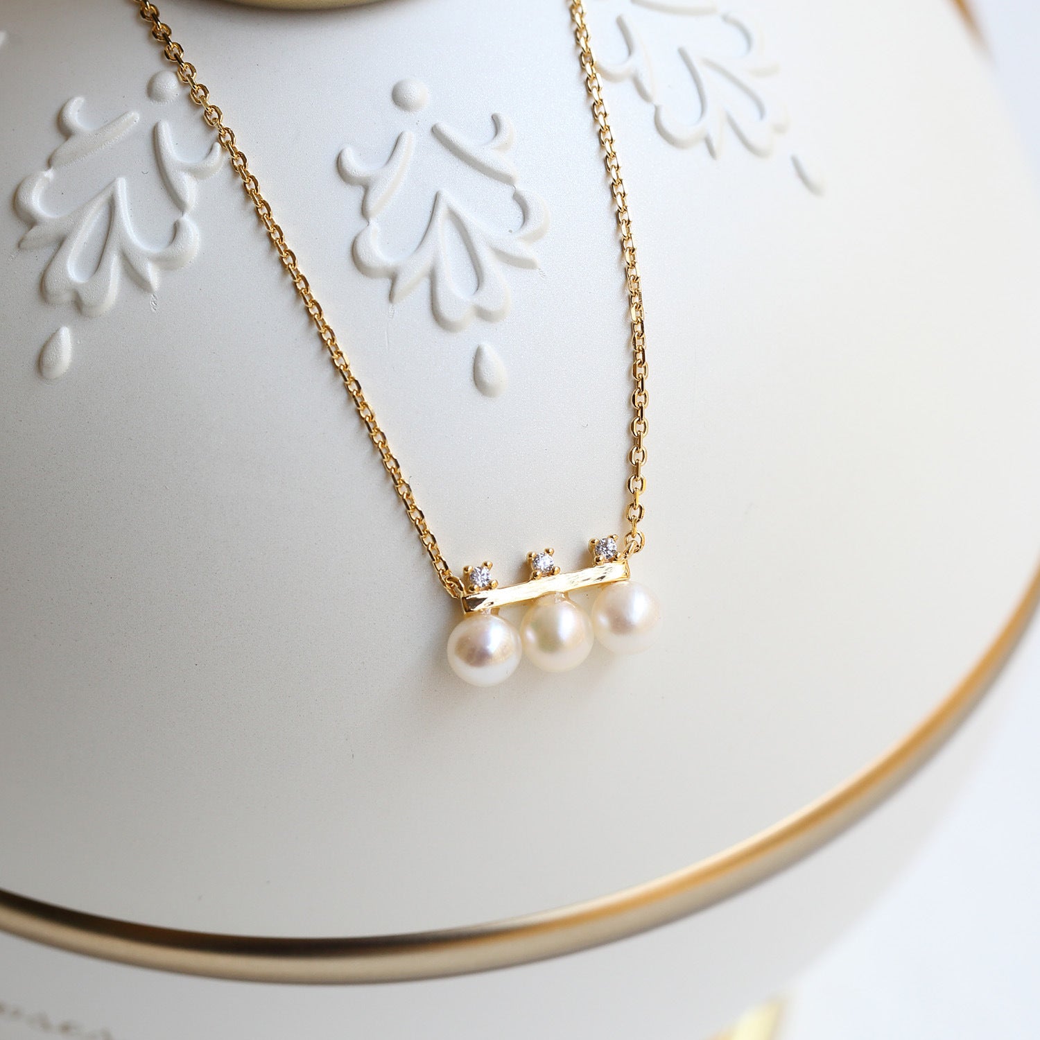 Gold necklace with pearls on a decorative white surface from Gembee Jewellery