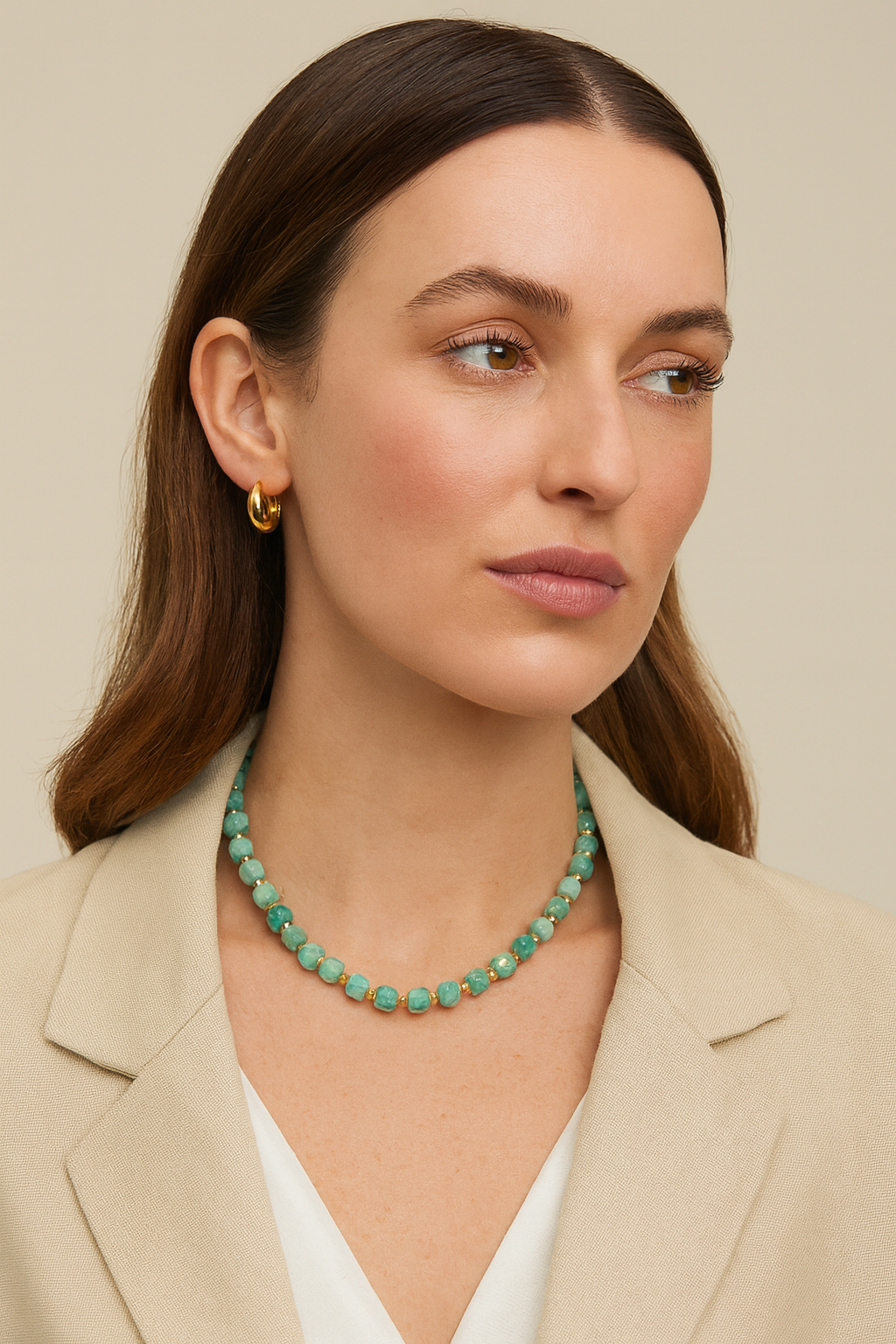 Woman wearing a green beaded necklace and gold earrings against a beige background