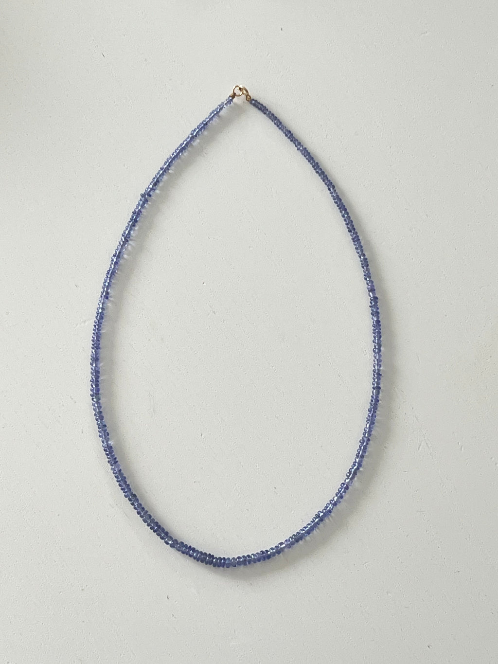 Thin tanzanite beaded necklace on a light gray background