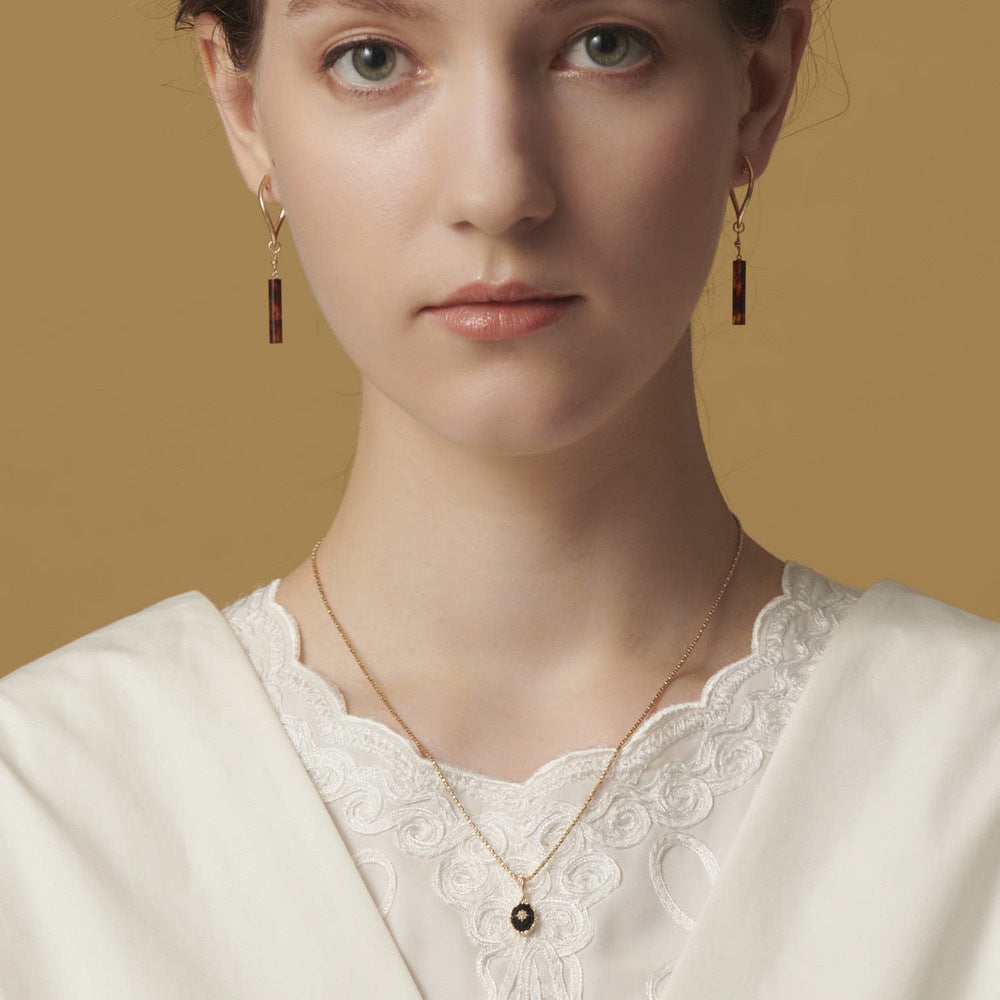 Woman wearing gold earrings and a necklace from  the GemBee Jewellery against a beige background